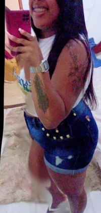 This lively live wallpaper features a fashionable woman taking a mirror selfie while wearing trendy denim shorts and Shipibo tattoos, set against a colorful tachisme background