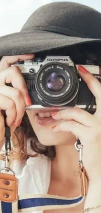 This phone live wallpaper displays a photorealistic depiction of a fashionable woman taking a picture with a vintage Olympus camera