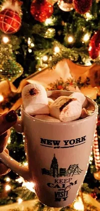 This live wallpaper features a festive scene of a person holding a cup of hot chocolate in front of a Christmas tree in New York City
