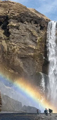Choose a stunning live wallpaper for your phone featuring a group of people standing near a breathtaking waterfall in the USA, surrounded by lush greenery and fishing boats navigating the river