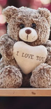 This phone live wallpaper features a lovable teddy bear clutching a heart with "i love you" inscribed in bold red letters