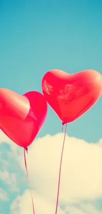 This phone live wallpaper features two heart-shaped balloons drifting across a blue sky