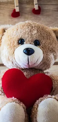 This delightful live wallpaper showcases a charming brown teddy bear hugging a red heart against a wooden background