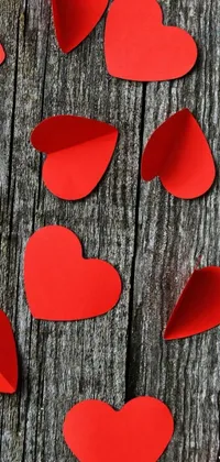 Looking for a romantic and charming live wallpaper for your phone? Look no further than this trending background image featuring a bunch of beautiful red paper hearts on a wooden table