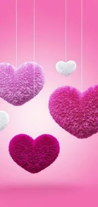 This phone live wallpaper features a group of hearts hanging from strings on a soft pink background