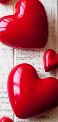 This phone live wallpaper showcases a stunning image of a group of red hearts arranged neatly on top of a wooden table