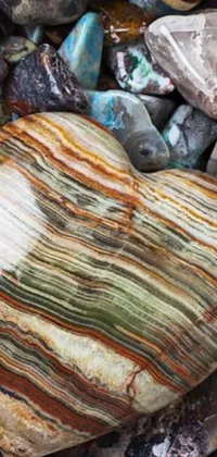 This live wallpaper is a stunning capture of a heart shaped stone resting on a pile of multi-colored rocks, boasting intricate geological strata and textured stripes