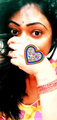 This phone live wallpaper showcases a heart-shaped image held close by a person wearing a colorful traditional Bihu dress called Mekhela Sador
