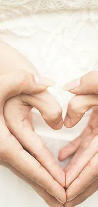 This phone live wallpaper features a stunning close-up shot of hands forming a heart gesture