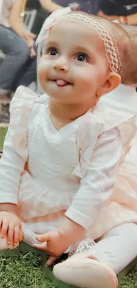 This live wallpaper showcases a charming baby dressed in white and light-pink attire, sitting gracefully before a mirror