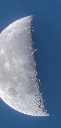 This phone live wallpaper presents a captivating close-up of a half moon against a clear blue sky