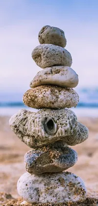 This phone live wallpaper showcases a stunning photograph of a rocky totem formation on a sandy beach