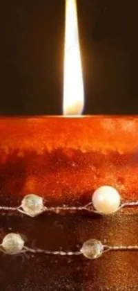 This phone live wallpaper features a beautifully lit candle sitting atop a glazed ceramic table, decorated with strings of pearls and amber jewels