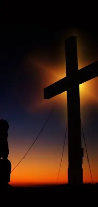 This phone live wallpaper showcases a serene image of a man kneeling in front of a wooden cross at sunset