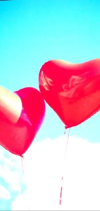 This live phone wallpaper features two heart-shaped balloons floating in a bright blue, sunny sky