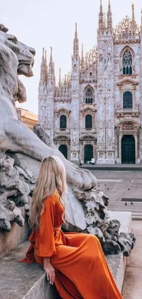 This phone live wallpaper showcases a beautiful woman in an orange dress situated on a bold stone lion statue