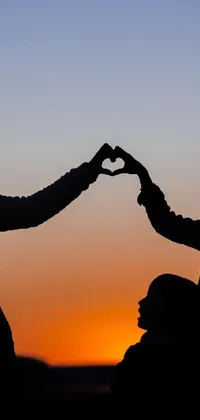 This live wallpaper showcases a heartwarming image of two individuals forming a heart shape with their hands on a sunset