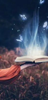 This magical live wallpaper features digital art by Anna Haifisch, depicting an open book held in a field, surrounded by glowing butterflies and a magic spell icon
