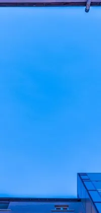 This phone live wallpaper features a sleek and modern building against a vibrant blue sky with fluffy clouds, accented by a postminimalism artistic style
