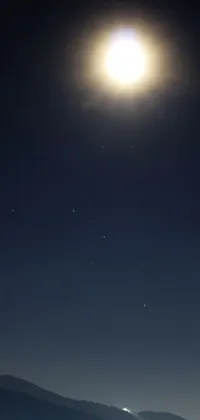 This phone live wallpaper depicts a serene scene of a man sitting on top of a lush green field under a full moon