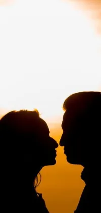 This phone live wallpaper showcases a romantic scene of a man and a woman sharing a gentle kiss in front of a stunning sun