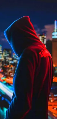 This phone live wallpaper features a dark and brooding figure in a hoodie looking out over a neonpunk city at night