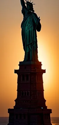 This phone live wallpaper depicts the Statue of Liberty as a silhouette against a beautiful setting sun