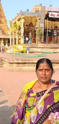 This mobile live wallpaper shows a mesmerizing image of a woman dressed in a vibrant yellow sari standing in front of a beautifully designed temple