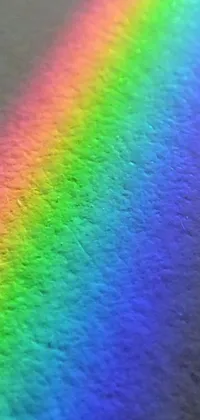 This phone live wallpaper features a close up of a rainbow on a table with holographic effects, fine stippling of light, and shimmering pigment particles