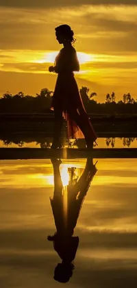 This stunning phone live wallpaper depicts a woman walking across a beautiful body of water at sunset