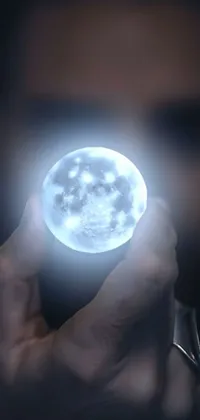 This phone live wallpaper is a captivating and mystical image of a man holding a holographic moon in front of his face