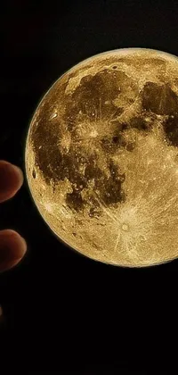 This live wallpaper features a stunning digital art of a yellow full moon placed atop a person's hand