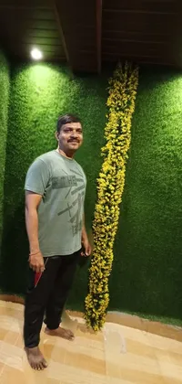 This phone live wallpaper depicts a man standing in front of a lush green wall covered in intricate moss and flowers