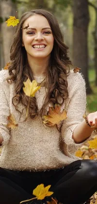 This phone live wallpaper features a serene brunette fairy woman sitting on top of a pile of autumn leaves