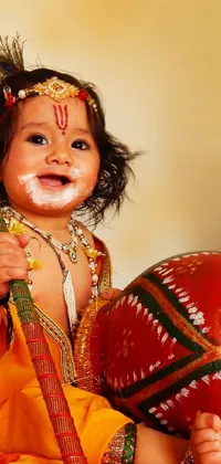 Experience India's rich culture with this captivating live wallpaper for your phone! The design features a sweet baby sitting on a comfy bed, clutching a vibrant red ball in their hands