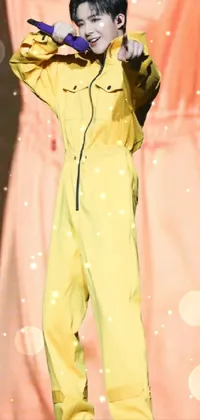 This live phone wallpaper depicts a man standing on stage with a microphone, clad in a vibrant yellow jumpsuit and air force attire