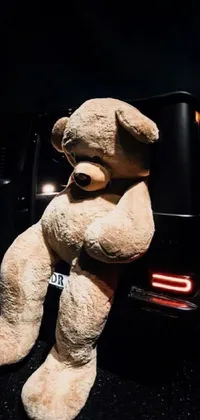 This live wallpaper for your phone features a charming and adorable scene of a large teddy bear sitting on the back of a car