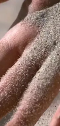 This live phone wallpaper showcases a stunning close-up of a hand holding sand
