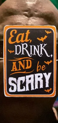 This phone live wallpaper features a Halloween-themed scene with a man holding a sign that says "Eat, Drink, and Be Scary" surrounded by images including a picture, front trading card, and die-cut sticker
