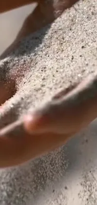 This live wallpaper showcases a close-up of sand flowing through a person's hands against a beautiful angle shot