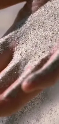This live wallpaper features a close-up shot of someone holding sand in their hands