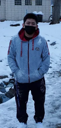 This phone live wallpaper depicts a man in a snowy landscape wearing a face mask and standing by a body of water, all while clad in a cozy hoodie