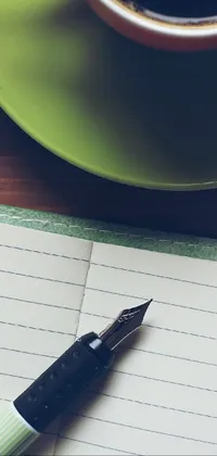 This live phone wallpaper features a close-up photo of a pen resting on top of a notebook alongside a cup of coffee