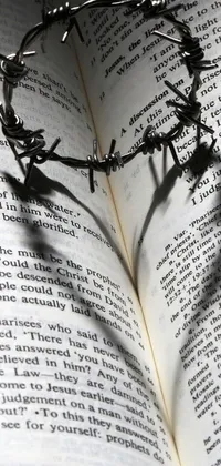 This phone live wallpaper showcases a captivating crown made of barbed wire resting atop an open book