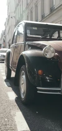 Get a glimpse of old-world charm with this vintage live wallpaper featuring an old car parked on the side of the road