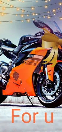 This live wallpaper features a photo-realistic image of an orange motorcycle parked on a roadside