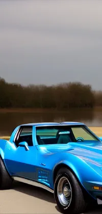 Get ready to elevate your phone's wallpaper game with this stunning live wallpaper featuring a beautiful blue 1969 Corvette C2 parked next to a serene body of water