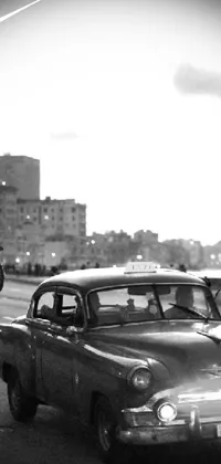 This phone live wallpaper showcases an old, black and white photo of a classic car with intricate details, set against a colorized vaporwave sunset background