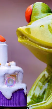 Looking for a fun and playful live wallpaper for your phone? Check out this cute green frog holding a colorful birthday cake! With its elephant-like trunk and happy expression, this cartoonish figurine is sure to bring a smile to your face