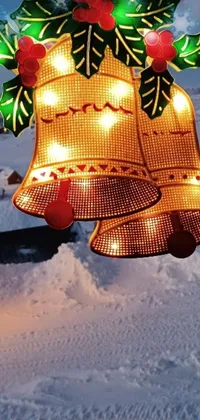 This phone live wallpaper features a lighted bell on a snow covered ground, complete with glowing lamps and snowflakes falling in the background